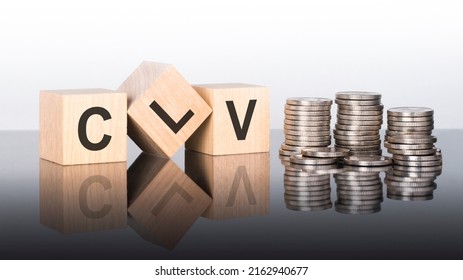clv - text is made up of letters on wooden cubes lying on a mirror surface, gray background. stacks with coins. inscription is reflected from the surface. clv - short for Customer Lifetime Value