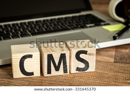 CMS (Custom Management System) written on a wooden cube in front of a laptop