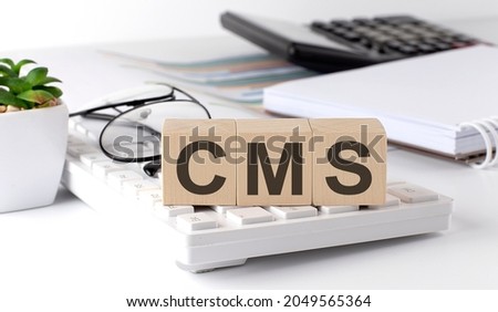 CMS written on a wooden cube on the keyboard with office tools