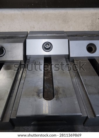 CNC machine vice and workholding fixture mounted on milling machine table in industrial workshop. Metalworking vice used for precision machining, engineering and manufacturing process. Industrial tools and equipment in factory.