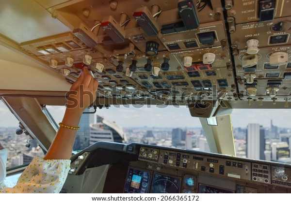 Co pilot hand control switch on\
over head panel in commercial airplane flying over city\
building