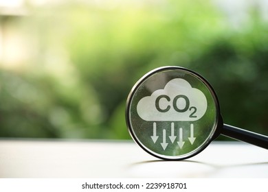 CO2 reducing icon inside magnifier glass on greenery background for decrease CO2 , carbon footprint and carbon credit to limit global warming from climate change, Bio Circular Green Economy concept.