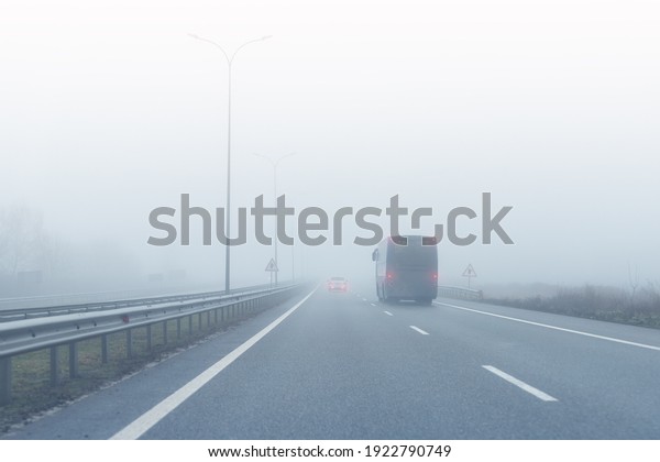 Coach bus on almost empty blue foggy misty rainy\
highway intercity road with low poor visibility on cold spring\
autumn morning. Seasonal bad rainy weather accident danger warning.\
car fog light