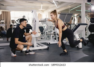 The Coach Checks The Correctness Of The Exercise On The Feet In The Gym. Training In The Gym Is A Small Group. A Man And A Girl Train Together.