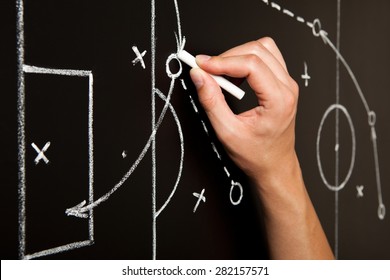 Coach drawing a football game tactics with white chalk on blackboard. Soccer coach explaining game strategy.