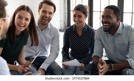 Coach or group leader telling funny story or joke to laughing diverse team. Happy multiethnic employees having fun while discussing project, sharing ideas, informal brainstorming sitting on chairs