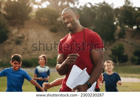Coach having a fun training session with kids in a school. PE teacher coaching a group of elementary school children. Sports education in primary school.