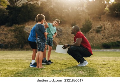 Coach having a team talk with a group of children in a school ground. Fitness trainer motivating a group of primary school kids. Sports and recreation in elementary school. - Powered by Shutterstock