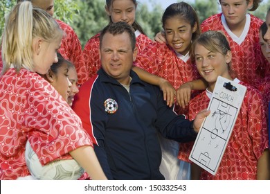 Coach Holding Clipboard While Discussing Strategy With Girls Soccer Team