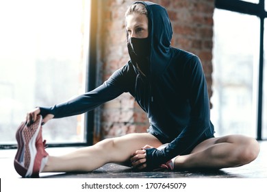 Coach Pilates In A Black Hoodie And Mask Making Exercise Stretching Leg Muscles
