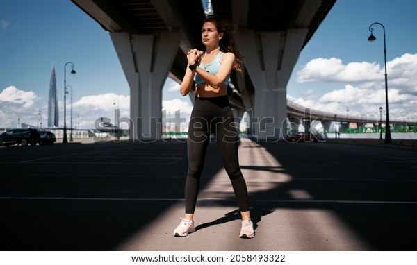 The coach\
is preparing for a marathon at a distance. Fitness training on the\
street in the city. A woman does warm-up and running exercises.\
Health, lifestyle,\
self-confidence.