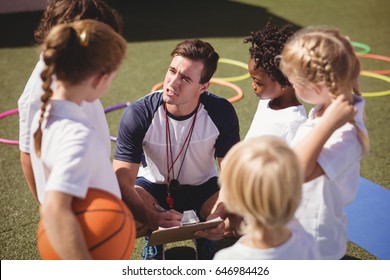 Coach and schoolkids discussing on clipboard in schoolyard - Powered by Shutterstock