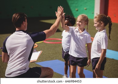 Coach and schoolkids giving high five to each other in schoolyard - Powered by Shutterstock