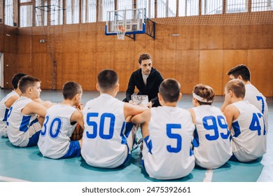 A coach is seen discussing a basketball strategy with kids seated on the gym floor, highlighting the sport's team aspect - Powered by Shutterstock