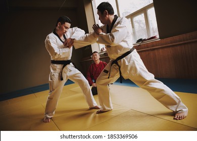 The coach sits on his knees while the two students fight in a scrum. Two men in white kimono fight in a karate hall.  - Powered by Shutterstock