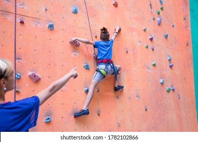 A coach teaches a child, a woman is belaying her son, a boy and his mother train together, children's climbing training, a boy climbs the wall, climbing gym - Powered by Shutterstock