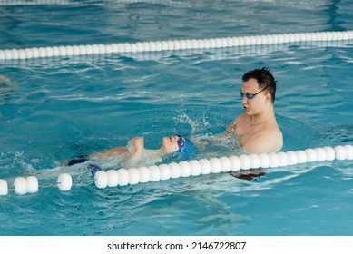 A coach teaches a seven-year-old boy to swim in a modern swimming pool. Learn to swim. Development of children's sports. Healthy parenting and promotion of children's sports