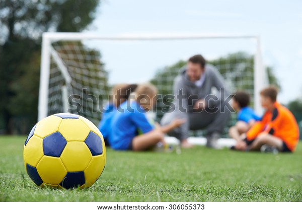 Coach  And Team Discussing Soccer Tactics With\
Ball In Foreground