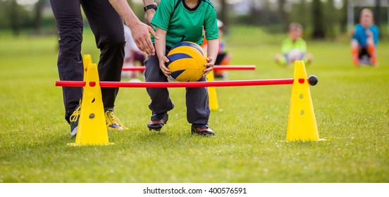 Coach And Young Boy Exercising With Ball On A Green Grass