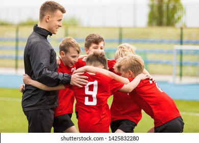 Coaching Youth Sports. Kids Soccer Football Team Huddle With Coach. Children Play Sports Game. Sporty Team United Ready To Play Game. Youth Sports For Children. Boys In Sports Jersey Red Shirts