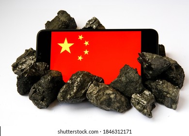 China’s coal addiction. Concept. Chinese industry and technology rely on coal and coal mining. Flag of China seen on the smartphone surrounded by the coal rocks. 