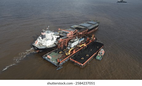 Coal barge loading operation using a floating crane to vessel in open waters off Banjarmasin, Indonesia.