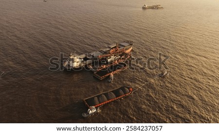 Coal barge loading operation using a floating crane to vessel in open waters off Banjarmasin, Indonesia.