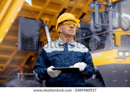 Coal mining worker use tablet computer on background big yellow truck.