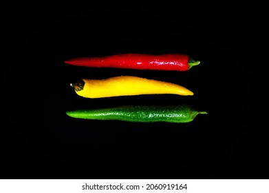 Coalition in red, yellow and green: Spicy threesome of fresh chilli pods against black background. Table top view, flat lay, copy space. - Shutterstock ID 2060919164