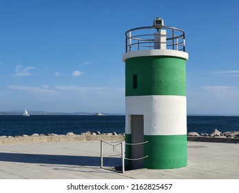 Coast of Atlantic ocean, location at the mouth of the Tagus River and green white cylindrical building - lighthouse next to Oeiras marina. Farol do Bugio or Forte de São Lourenço visible away.