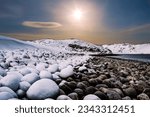 The coast of the Barents Sea with boulders covered with snow and snow-capped mountains on the horizon. Winter landscape. Russia