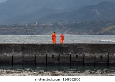 Coast Guard Personnel On A Routine Patrol In Chenggong Harbour Taiwan. Life Safety And General Public Safety Illustration, Looking Over The Edge Of A Concrete Wall, Checking The Water Below For Debris