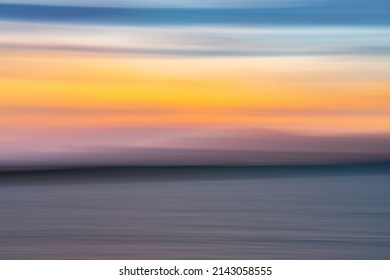 Coastal background image of sunset colors on water and in sky above horizon.