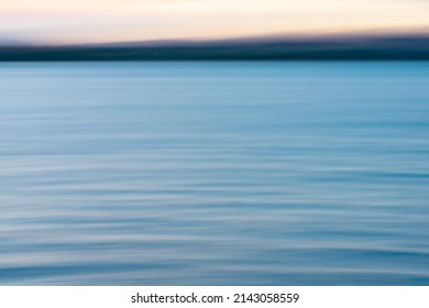 Coastal background image of sunset colors on water and in sky above horizon.