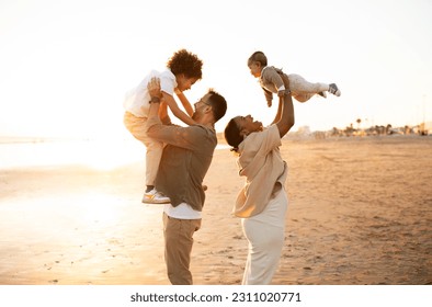 Coastal captures. Parents playing and having fun with their sons, throwing up boys in the air, spending time on the beach at sunset, side view, free space - Shutterstock ID 2311020771