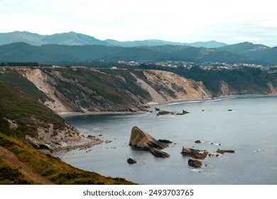 Coastal cliffs and rocky shore with distant mountains under overcast sky.  - Powered by Shutterstock