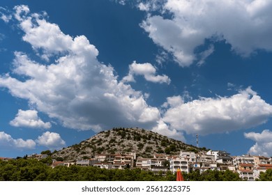 Coastal hillside village with green forest, anchored boats, and bright fluffy clouds in a blue sky on a sunny day. Concept of tranquil seaside living, nature, and leisure. High quality photo - Powered by Shutterstock