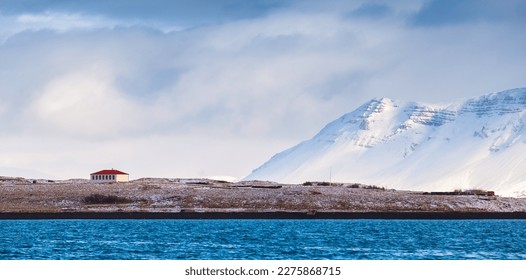 Coastal Icelandic landscape with residential house and snowy mountains under cloudy sky. Reykjavik district, Iceland - Powered by Shutterstock - Get 15% off with code: PIKWIZARD15