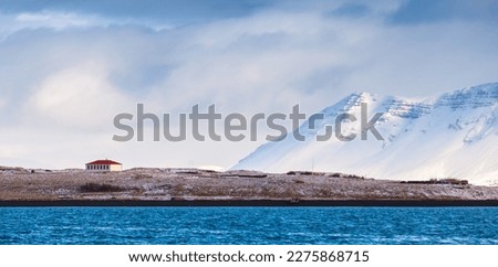 Coastal Icelandic landscape with residential house and snowy mountains under cloudy sky. Reykjavik district, Iceland