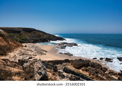 
Coastal landscape with rocky cliffs, sandy beach, and blue ocean waves under a clear sky. - Powered by Shutterstock