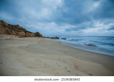 coastal landscape with a sandy beach stretching along the shoreline. The left side of the image showcases tall, golden cliffs with distinct layers of rock formations - Powered by Shutterstock