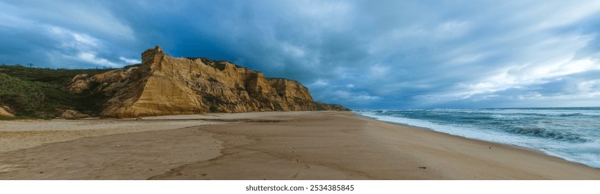 coastal landscape with a sandy beach stretching along the shoreline. The left side of the image showcases tall, golden cliffs with distinct layers of rock formations - Powered by Shutterstock