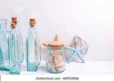 Coastal living  home decorations. Decorative bottles, starfish, shells  in ray of light on white textured background. Selective focus. Place for text.