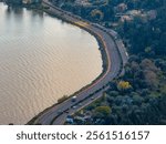 Coastal road winds along tranquil water, connecting urban and natural landscapes.