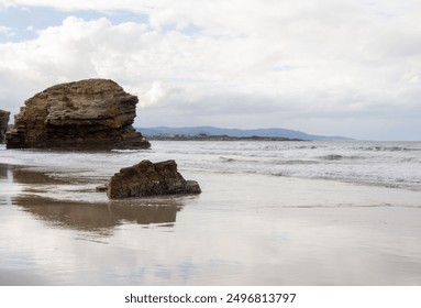 Coastal rock formation on sandy beach at sunset with ocean waves and lush greenery. Cathedral Beach, Lugo, Spain - Powered by Shutterstock