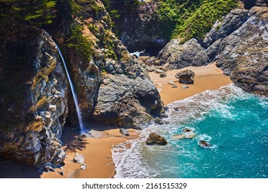 Coastal Rocks With Waterfall Releasing Onto Sandy Beaches Next To Ocean Cove