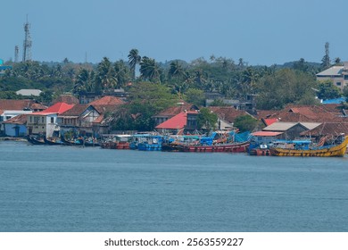 A coastal scene in India features vibrant fishing boats, red roofed buildings, and lush palm trees, with communication towers indicating a developed area. - Powered by Shutterstock