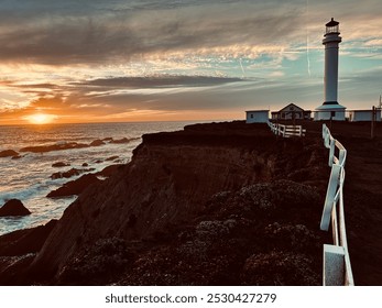 A coastal scene at sunset featuring a lighthouse on a cliff overlooking the ocean. The setting sun casts a warm glow over the ocean and rocky shoreline, creating a serene and dramatic atmosphere. - Powered by Shutterstock