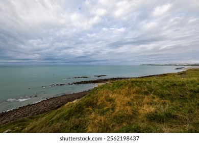 Coastal scenery with rocky shorelines, green cliffs, and a cloudy sky creates a dramatic and serene view of nature - Powered by Shutterstock