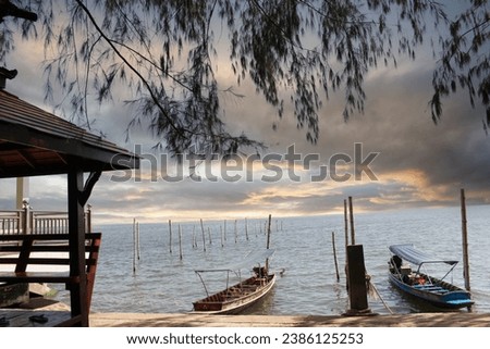 A coastal seascape featuring Thai-style long-tail boats docked at the pier, catering to tourists, surrounded by large trees.